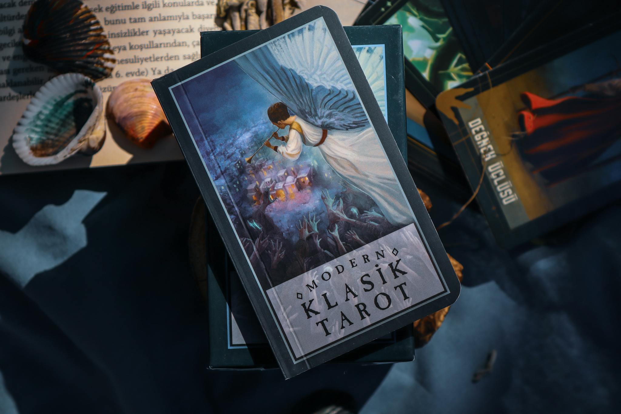 A close-up of modern tarot cards on a table with shells and shadows.